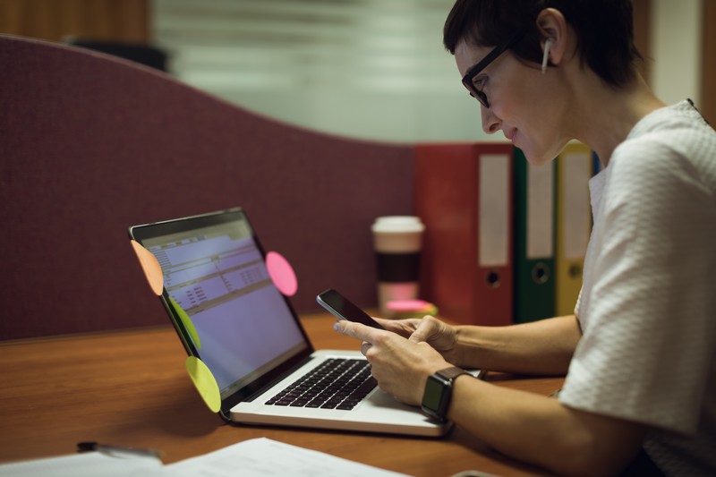 Businesswoman using mobile phone while working on laptop in office o que é notícia